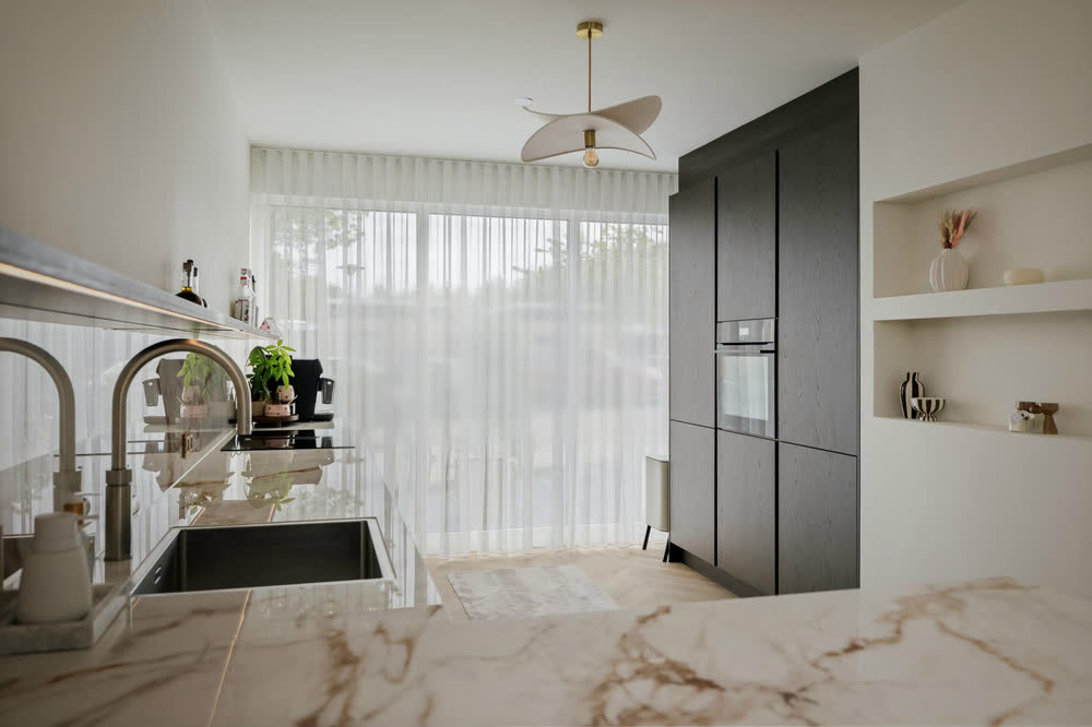 Keuken in Deventer: hoge kastenwand in donker fineer met inbouwoven, een licht werkblad in marmerlook met kokendwaterkraan en open nissen in de wand